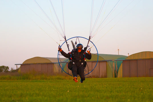 Person paragliding on a grassy field with buildings in the background