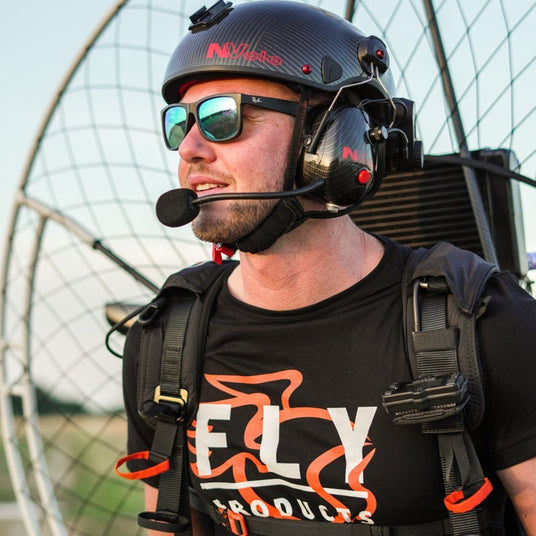 Person wearing a helmet and sunglasses with a headset, standing in front of a power kite.
