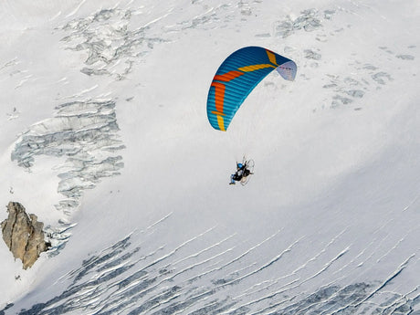 Person paragliding over a snowy mountain landscape