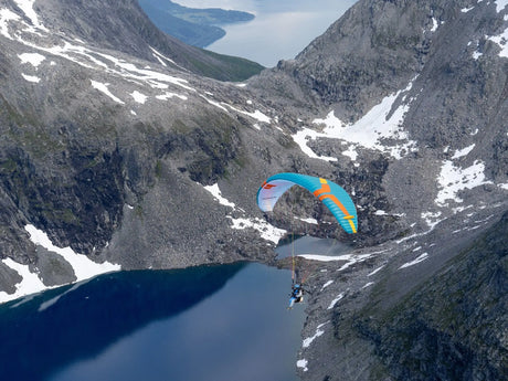 Paraglider flying over a mountainous landscape with a lake below