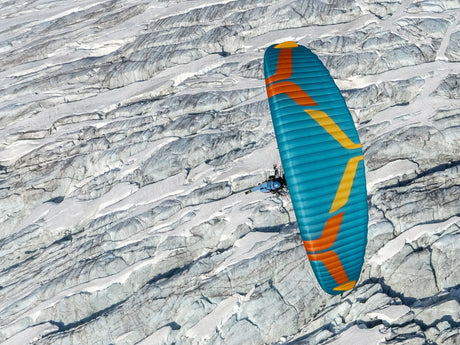 Blue and orange paraglider soaring over a rocky landscape