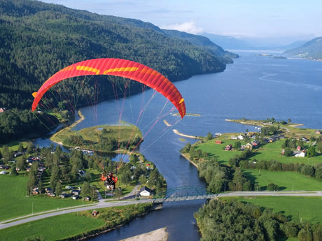Paraglider flying over a scenic landscape with a river and mountains.