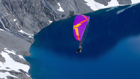 Person paragliding over a blue lake with mountains in the background