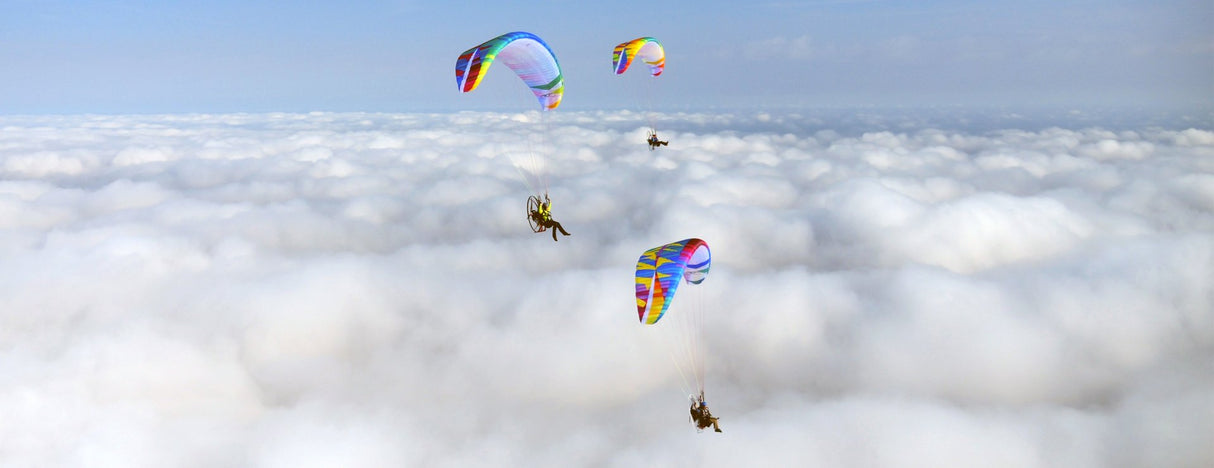 three paramotors flying above the clouds