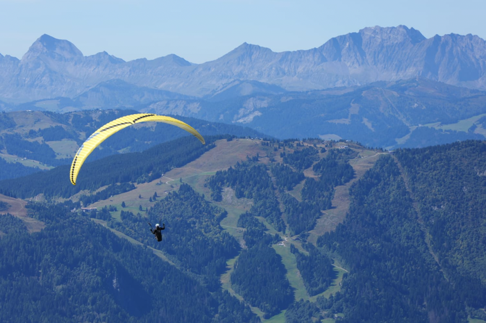 Person paragliding over a mountainous landscape with clear blue sky