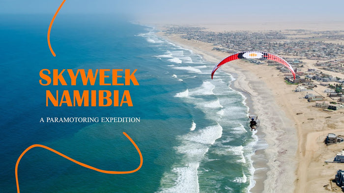 Aerial view of a beach with a paramotor flying over, promoting 'SKYWEEK NAMIBIA'.