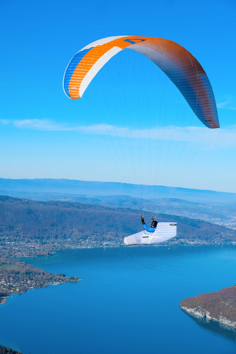 Person paragliding over a lake with a clear blue sky