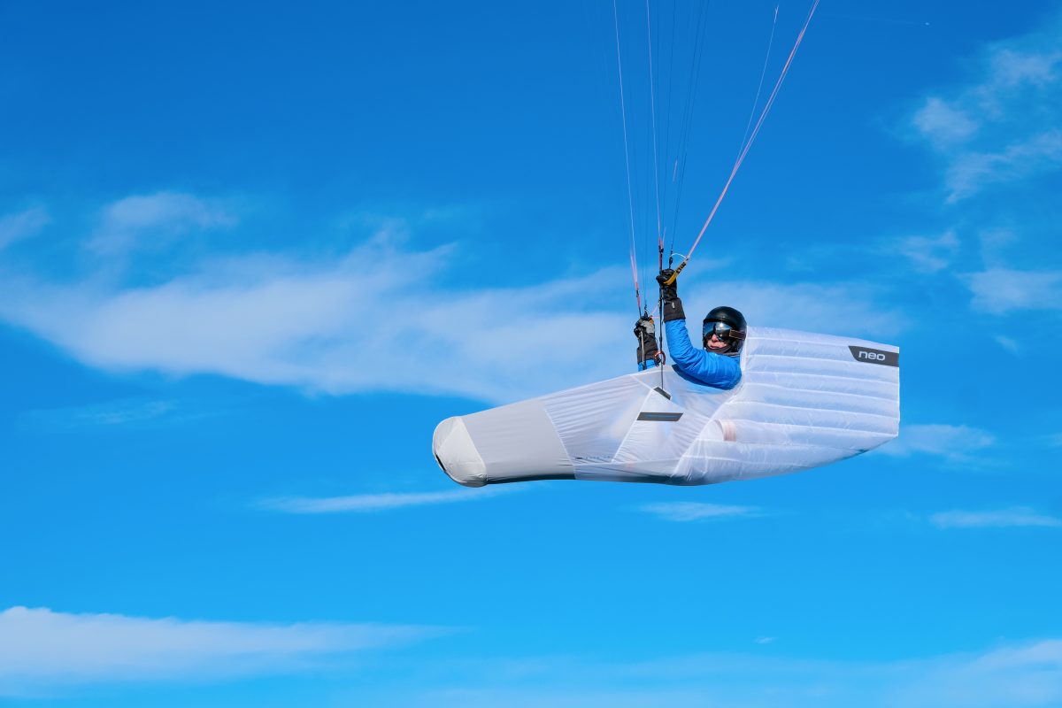 Person hand gliding in a clear blue sky with a white paraglider.