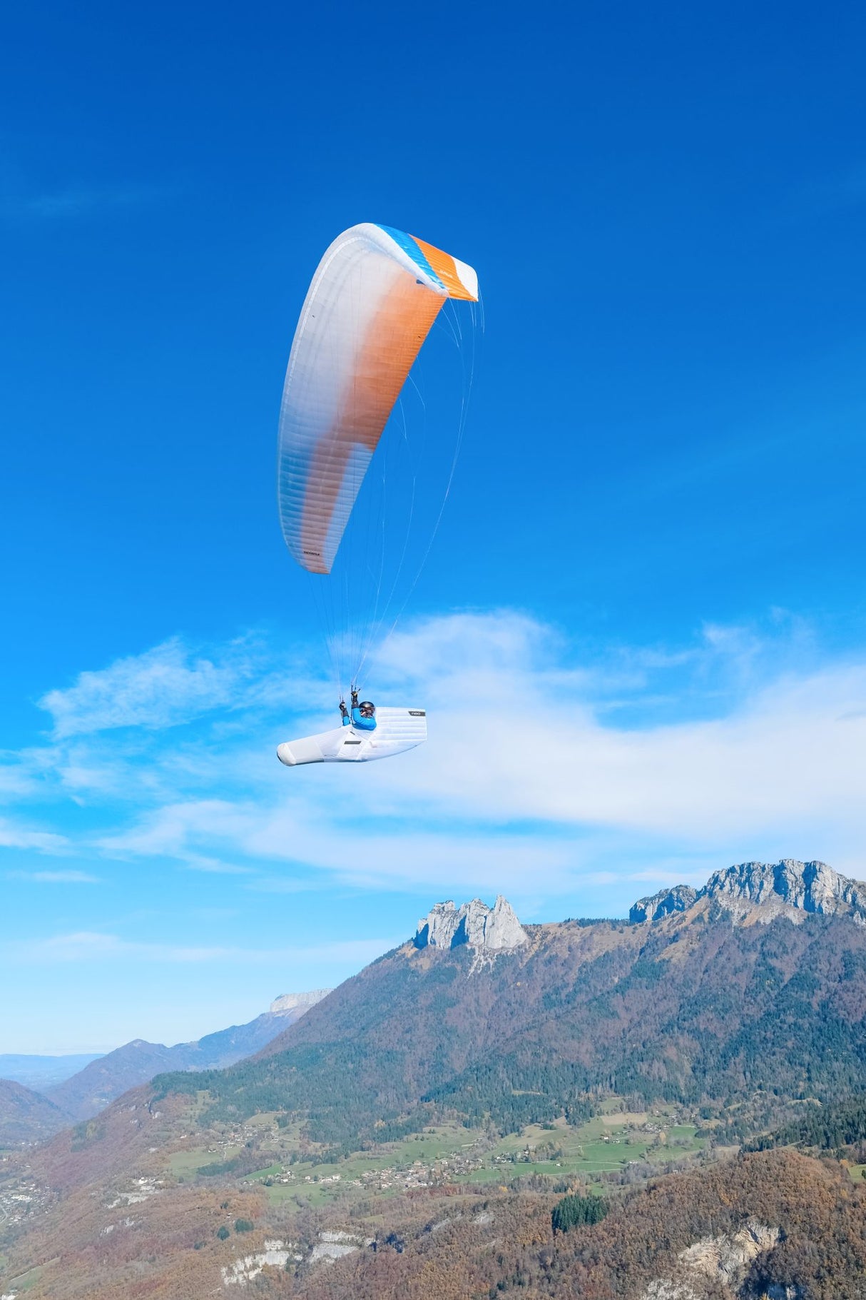 Person hand gliding over a mountainous landscape with a clear blue sky.
