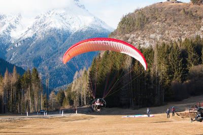 Paraglider in mid-flight with mountains and trees in the background